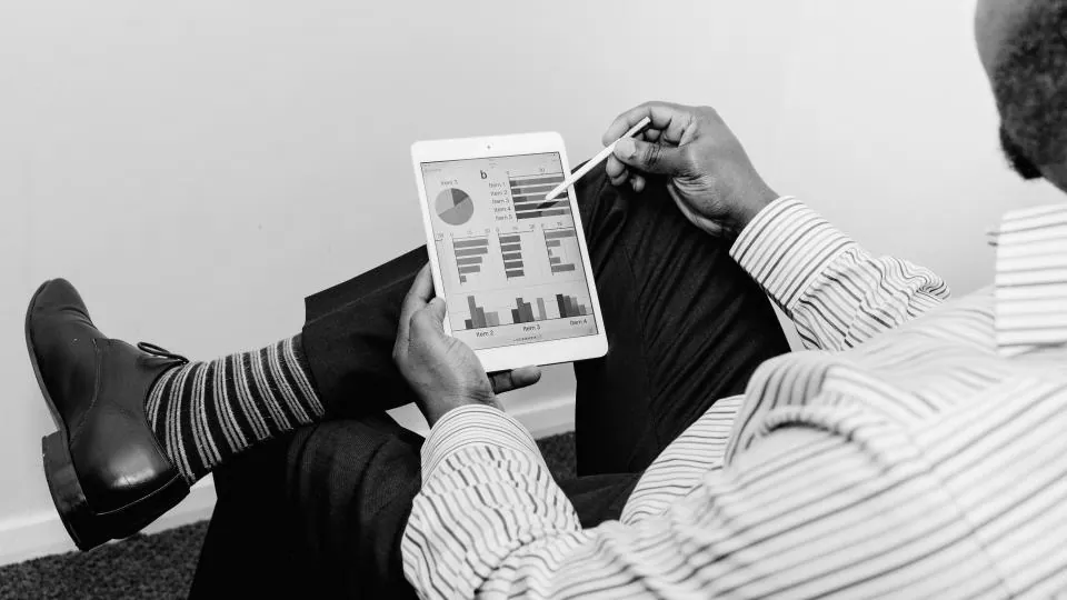 Executivo de terno, sem o rosto à mostra, lendo os gráficos de um relatório em um tablet
