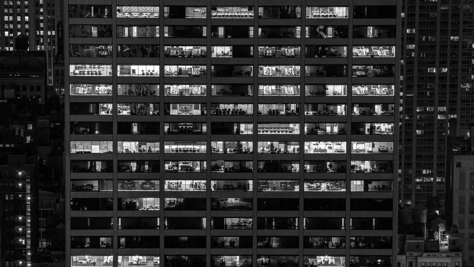 Fachada de um prédio de escritórios à noite, com dezenas de janelas acesas vistas de longe