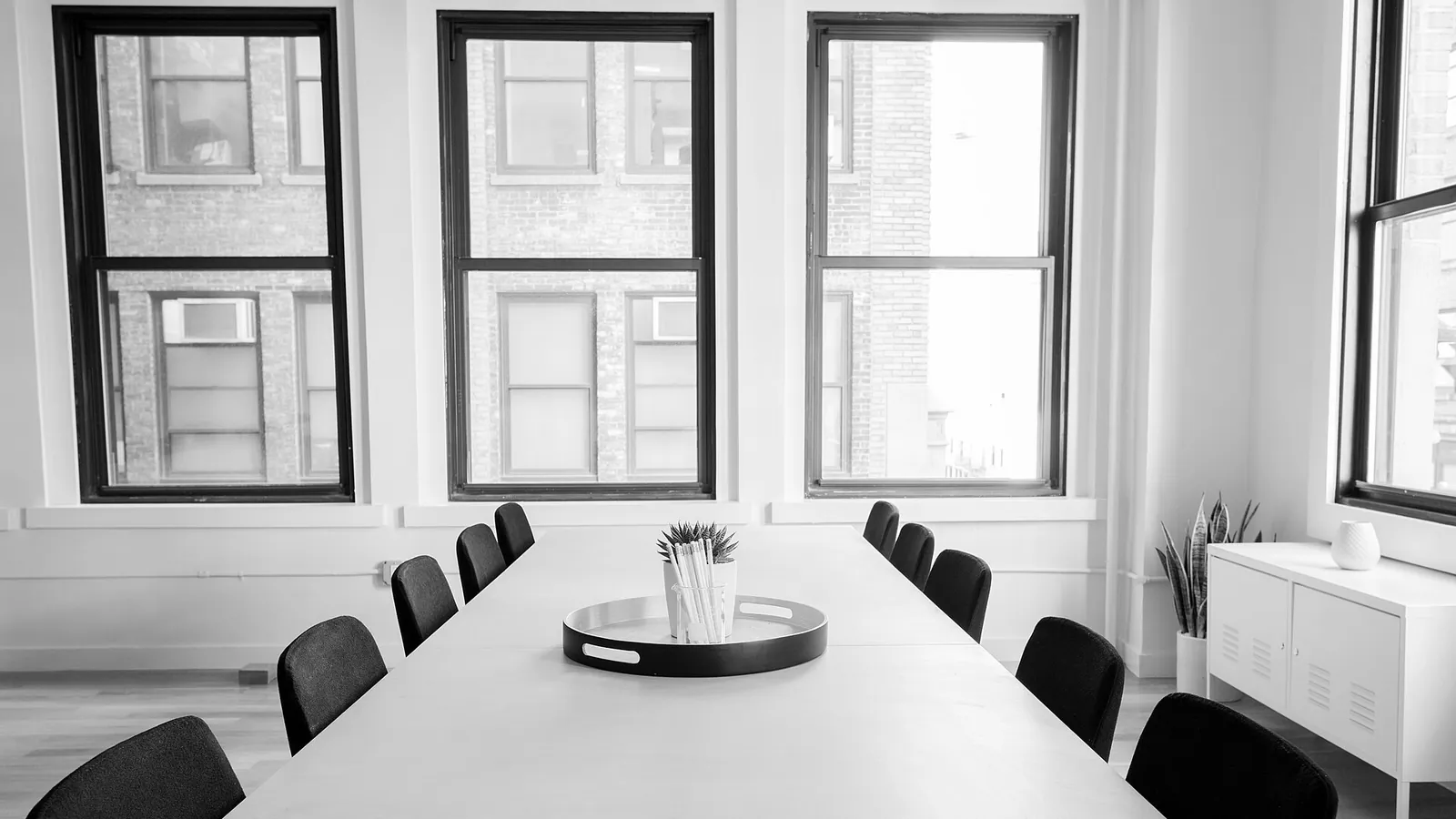 Sala de reunião vazia, com uma mesa comprida, cadeiras dos dois lados e janelas altas ao fundo