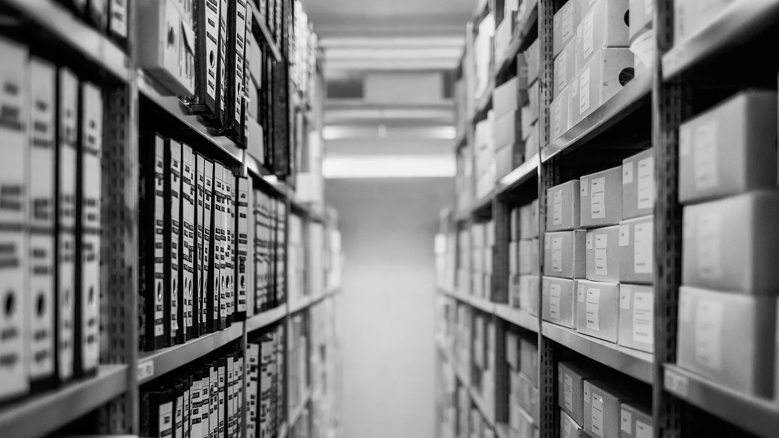 Corredor de um arquivo entre estantes de metal cheias de pastas e caixas de documentos
