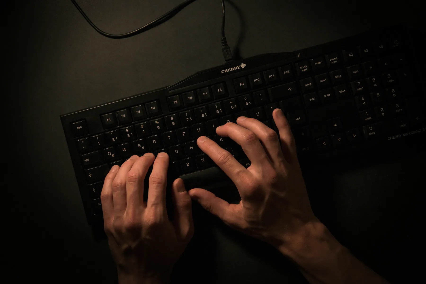 Mãos digitando em um teclado, em ambiente escuro