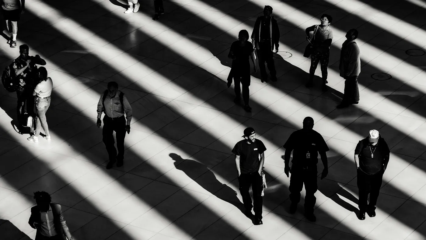 Pessoas caminhando entre faixas de luz e sombra